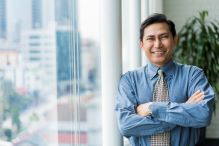 A formally dressed man next to a window smiling at the camera.