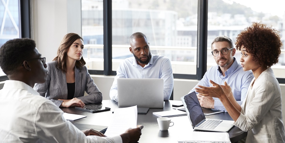 Office workers sitting around a table with their laptops and notebooks on the table