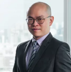 Bald man in a suit with glasses standing by a window.