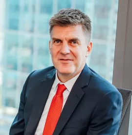 Man in a suit with a red tie sitting by a large window.