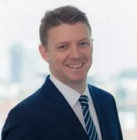Smiling man in suit and tie with blurred city background.