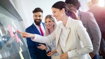 Business team collaborates around a glass board with sticky notes.