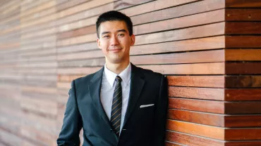 Asian man in a business suit standing against a wall
