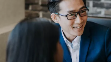 Person in a blue suit smiling during a conversation in a modern office.