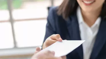 Woman in a suit handing a business card to another person.