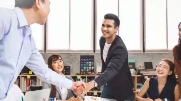 Group of coworkers in an office, two men shaking hands.