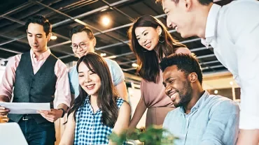 Group of colleagues smiling and working together around a laptop.