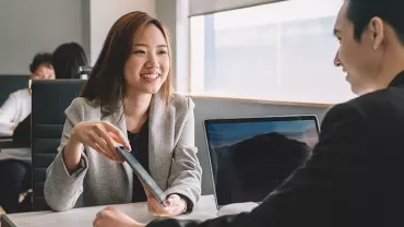 A woman is smiling and handing a document to a man in a modern office.