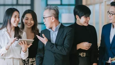 A group of professionals smiling and discussing with a tablet in an office setting.