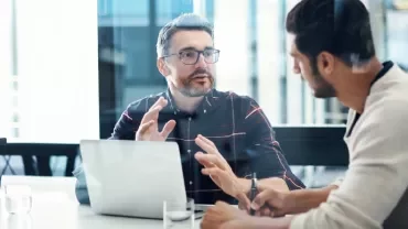 Two men having a discussion at a conference table with a laptop.