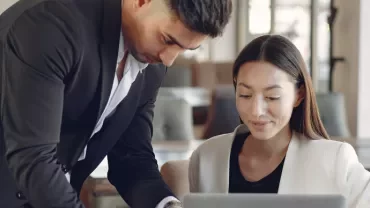 Man and woman collaborating on a laptop in an office.
