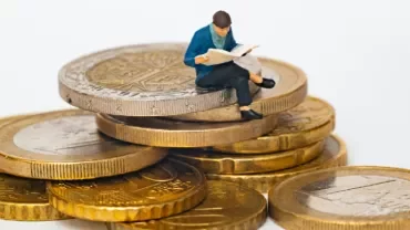 Miniature figure reading on stack of coins.
