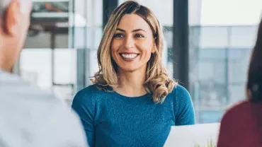 Woman in blue shirt smiling during a meeting.