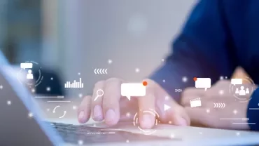 Person typing on a laptop with digital icons floating above the keyboard.