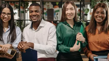 Four diverse young professionals smiling in an office setting.