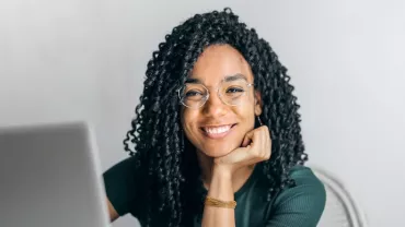 Smiling person with glasses sitting at a laptop.