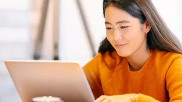 Woman in orange sweater using a laptop at home.