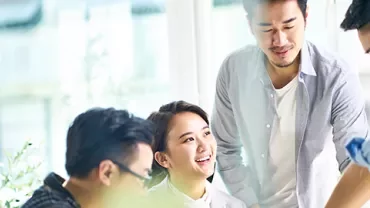 A group of four people having a meeting in a bright office space, with plants in the foreground.