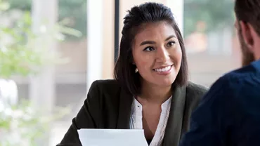Woman in a white shirt and blazer smiling at a man with a beard during a meeting.