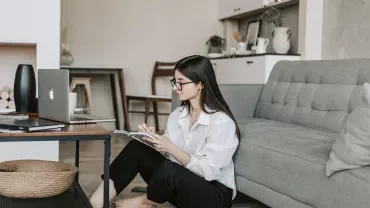 Woman sitting on floor by a coffee table with a laptop and notebook.