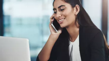 Woman smiling while talking on a phone and using a laptop.