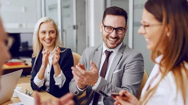 Group of people in formal attire smiling and clapping at a meeting.