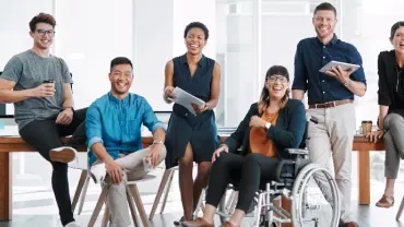 A diverse team of seven people smiling and posing in a modern office environment.