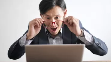 Surprised man with glasses looks at laptop