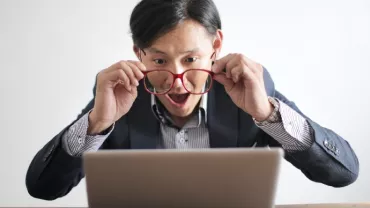 Surprised man with glasses looks at laptop