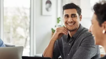Three people smiling and working on laptops in a bright office.