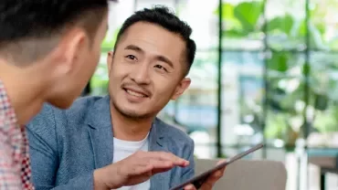 One male professional holding a tablet and in discussion with another male professional