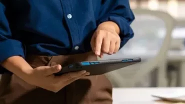 Individual displays a tablet in front of a laptop, illustrating the use of multiple technology tools.