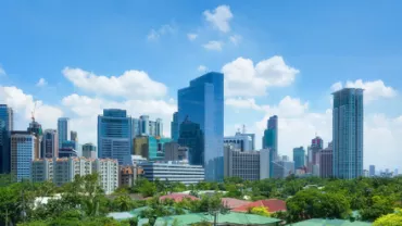 Skyline view of a city with modern skyscrapers and lush greenery under a clear blue sky.