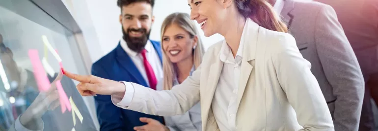 Business team collaborates around a glass board with sticky notes.