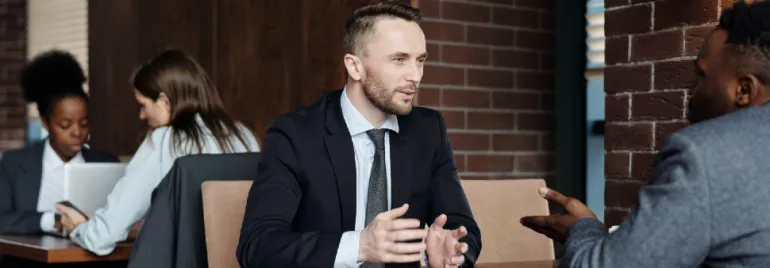 Two men in suits having a discussion at a table in a coffee shop.