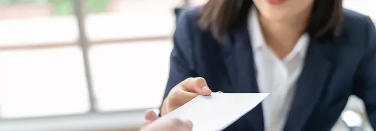 Woman in a suit handing a business card to another person.