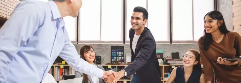 Group of coworkers in an office, two men shaking hands.