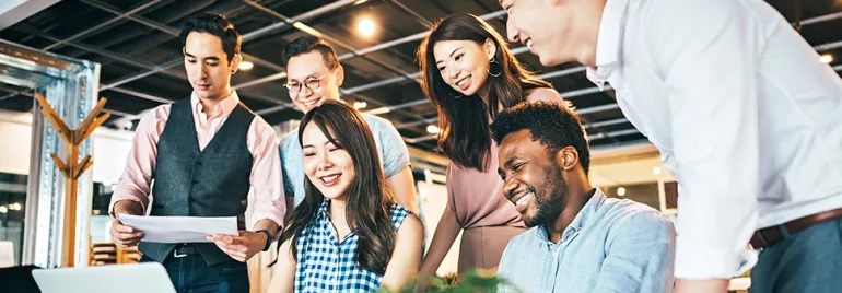 Group of colleagues smiling and working together around a laptop.
