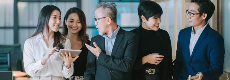 A group of professionals smiling and discussing with a tablet in an office setting.