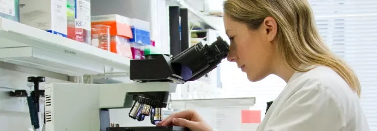 Scientist examining a sample through a microscope in a lab.