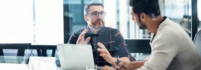 Two men having a discussion at a conference table with a laptop.