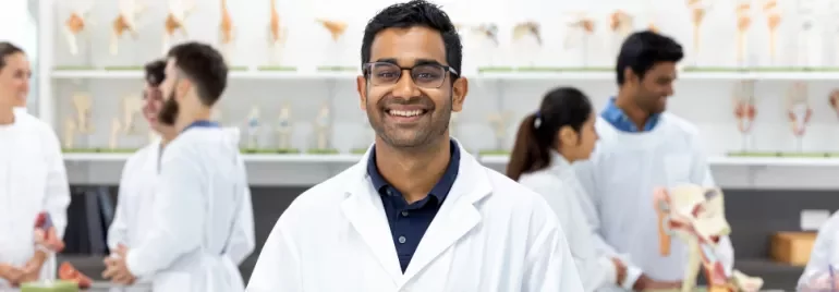 Smiling student in a lab coat in a classroom with anatomical models.