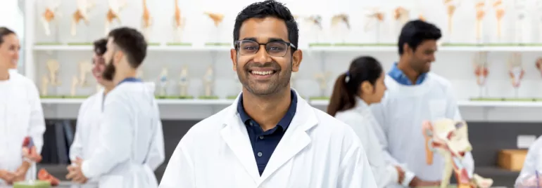 Smiling student in a lab coat in a classroom with anatomical models.