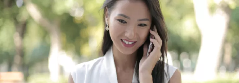 Woman smiling while talking on a mobile phone outdoors.
