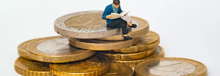 Miniature figure reading on stack of coins.