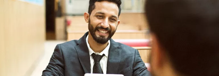 Smiling man in a suit holding a tablet, sitting at a table.