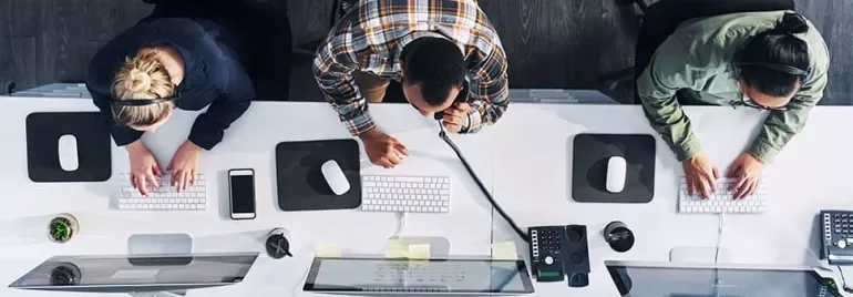 Top view of three people working at computers in an office setting.