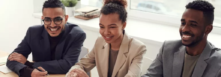 Three people sitting at a desk, smiling during a meeting.