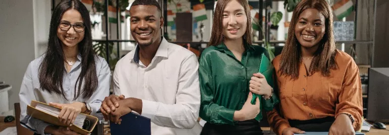 Four diverse young professionals smiling in an office setting.