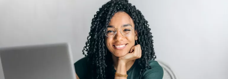 Smiling person with glasses sitting at a laptop.